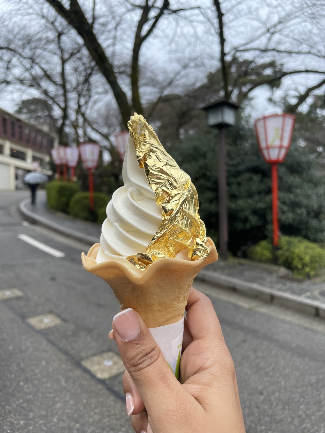 A soft-serve cone wrapped in a sheet of gold leaf, lanterns behind